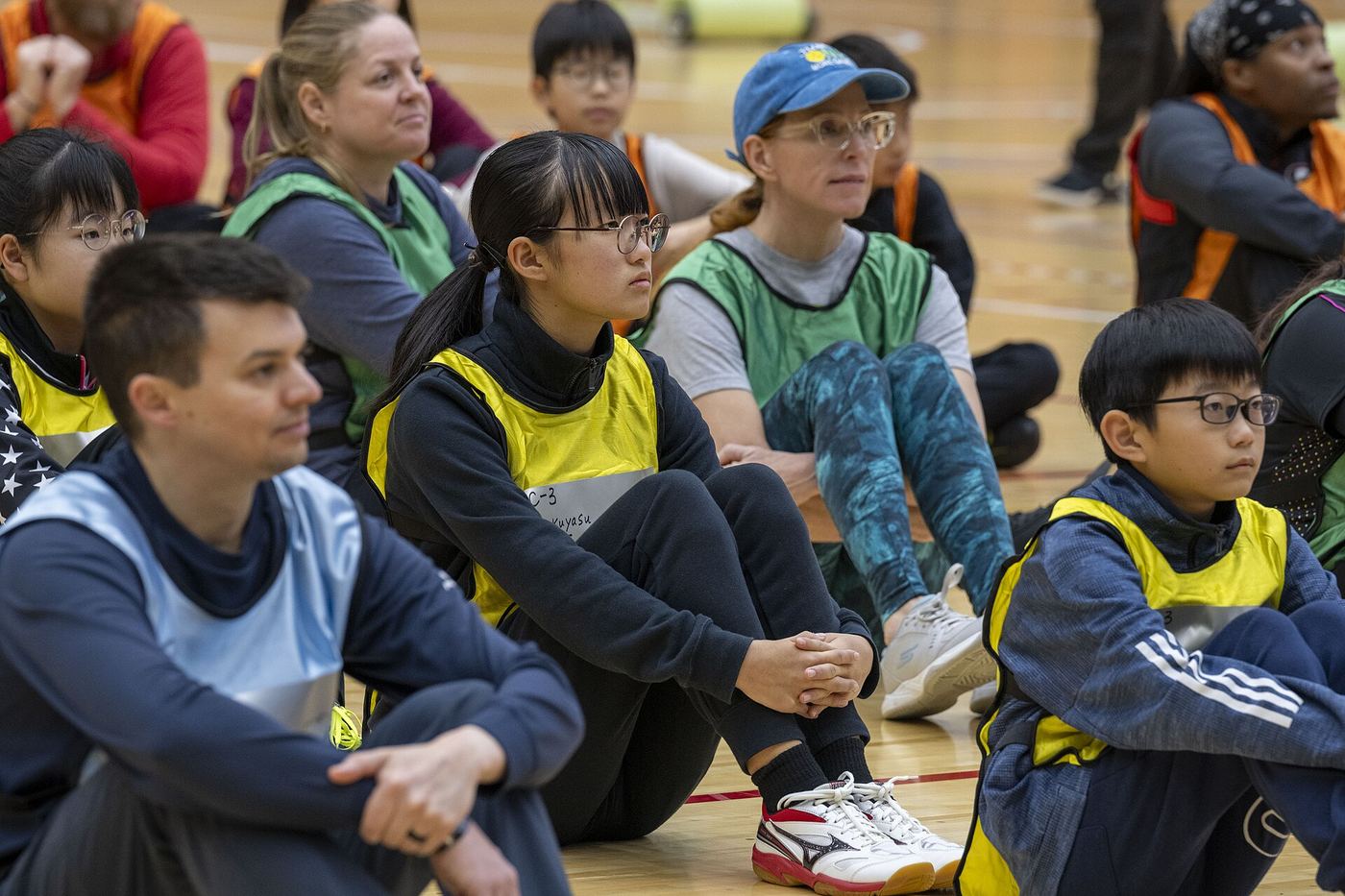 Kids and adults sit courtside together at a community pickleball event