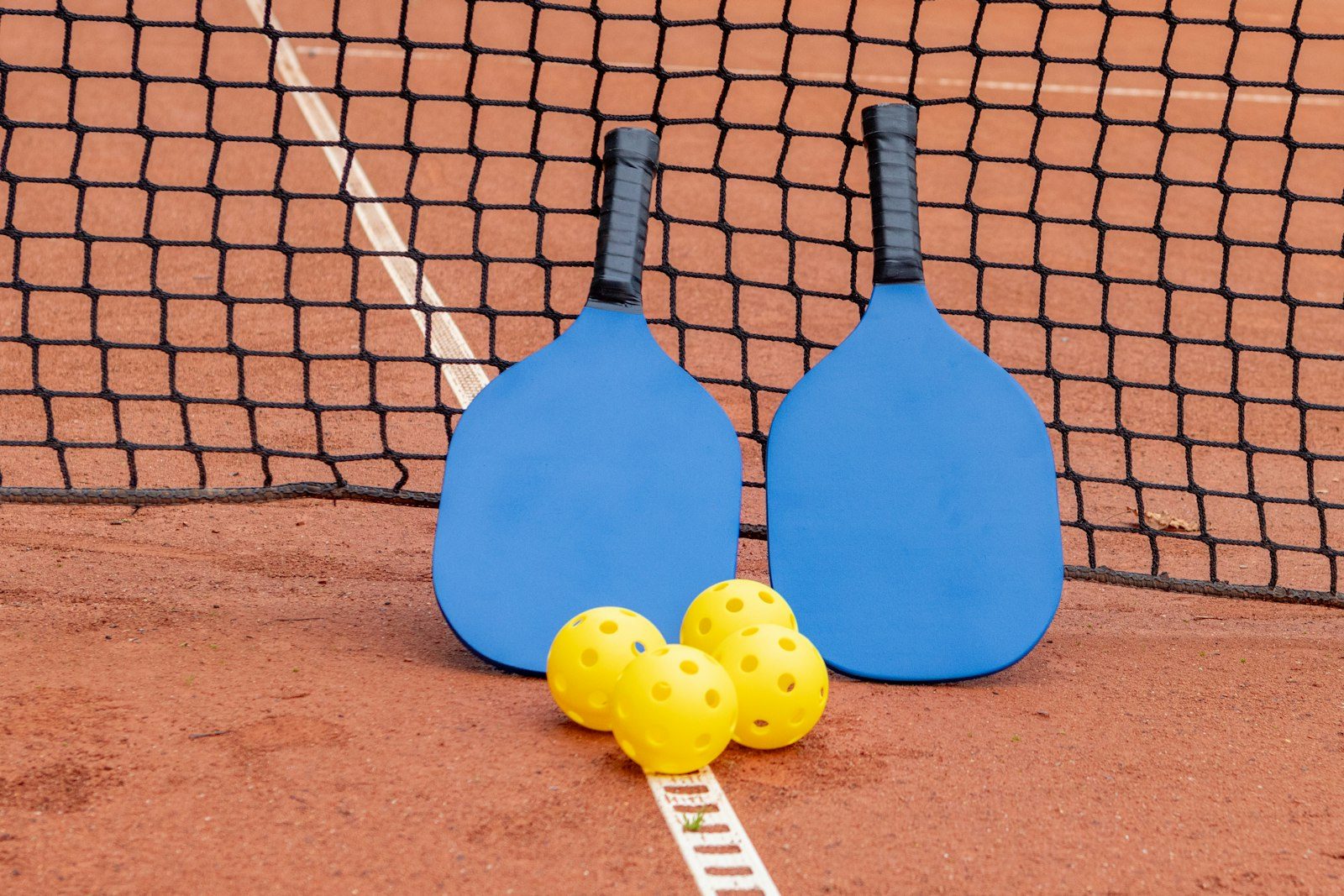 Two paddles and three pickleballs resting on a court